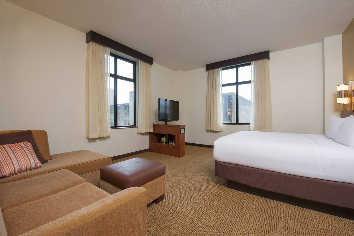 A hotel room with a bed, a sofa, a television, and a small cabinet.