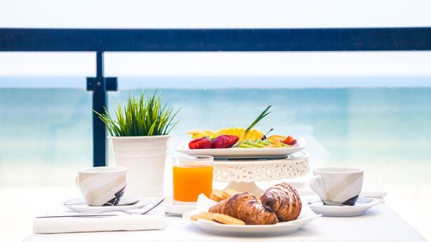 Desayuno con cruasanes, fruta y jugo en un balcón con vistas al mar.