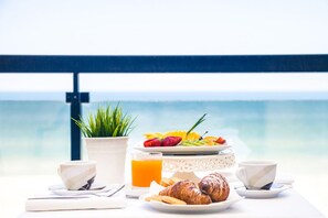 Desayuno con cruasanes, fruta y jugo en un balcón con vistas al mar.