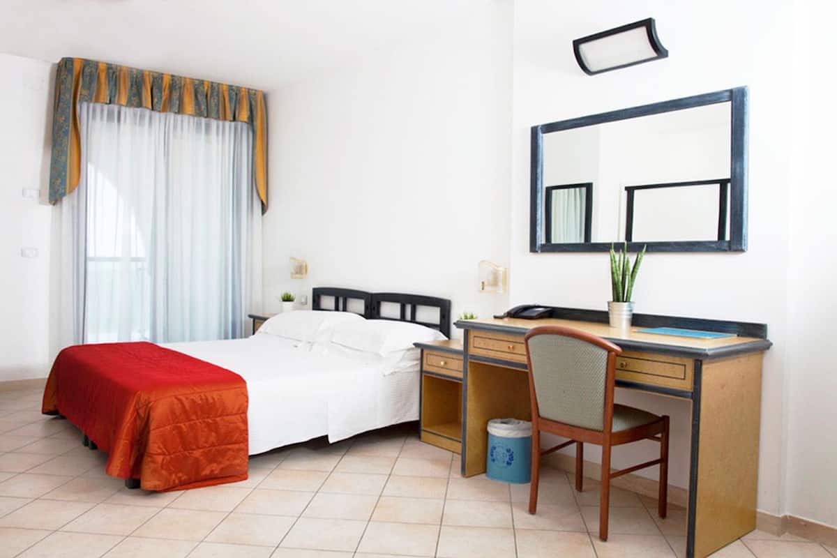 A hotel room with a bed, desk, chair, and a large mirror.