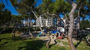 Un parque con juegos infantiles, árboles y un edificio con balcones al fondo.