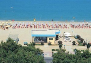 Una playa con hileras de sombrillas y sillas, una torre de salvavidas y un pequeño edificio con techo azul.