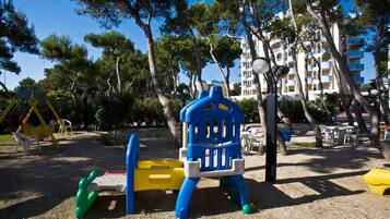 Ein Spielplatz mit einer blauen und gelben Spielkonstruktion, umgeben von Bäumen und einem Gebäude im Hintergrund.
