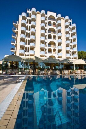 Un hotel con una piscina grande, varios balcones y zonas de estar al aire libre.