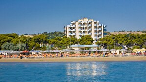 Un hotel costero con varios balcones, ubicación frente a la playa y vistas al mar.