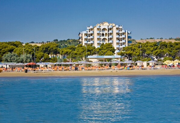 Un hotel costero con varios balcones, ubicación frente a la playa y vistas al mar.
