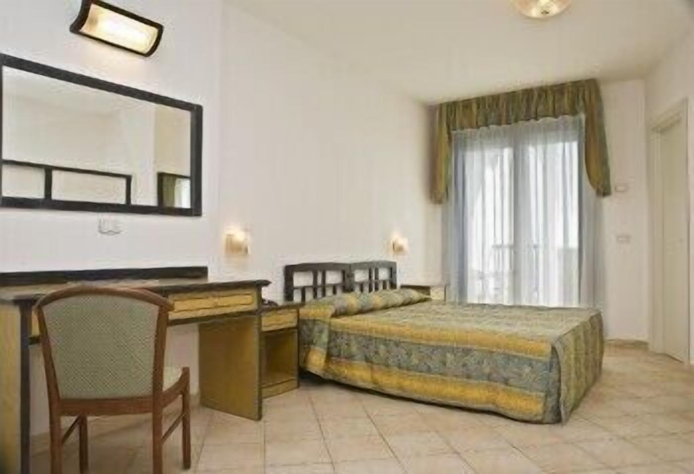 A hotel room with a bed, a desk, a chair, a mirror, and a window with curtains.