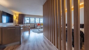 A modern hotel room with a wooden partition, a dining area with a round table, and a sofa. - Hotel Sporting (Pas de la Casa)