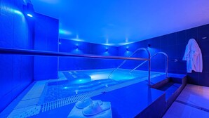 Un spa moderne doté d’un espace piscine éclairé de lumière bleue, d’un coin salon avec des serviettes à disposition et d’une douche visible.