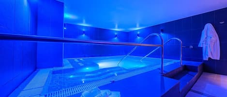 A modern spa with a blue-lit pool area, a seating area with a towel, and a visible shower.