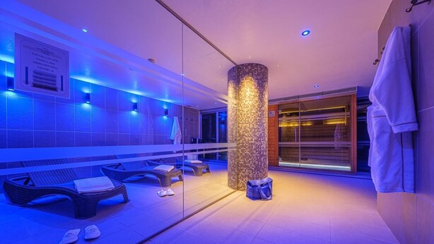 Un espace spa moderne doté d’un grand miroir, de fauteuils de relaxation en osier, d’un pilier en mosaïque et d’une cloison en verre.