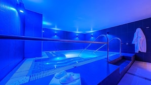 Un spa moderne doté d’un espace piscine éclairé de lumière bleue, d’un coin salon avec des serviettes à disposition et d’une douche visible.