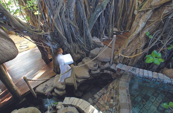 Una terraza de madera con barandilla de cuerda, un camino de piedra y una pequeña fuente.