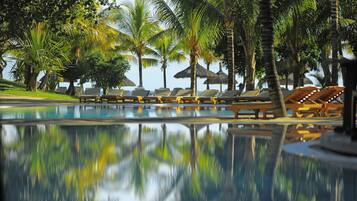 A pool area with lounge chairs and umbrellas, surrounded by palm trees.