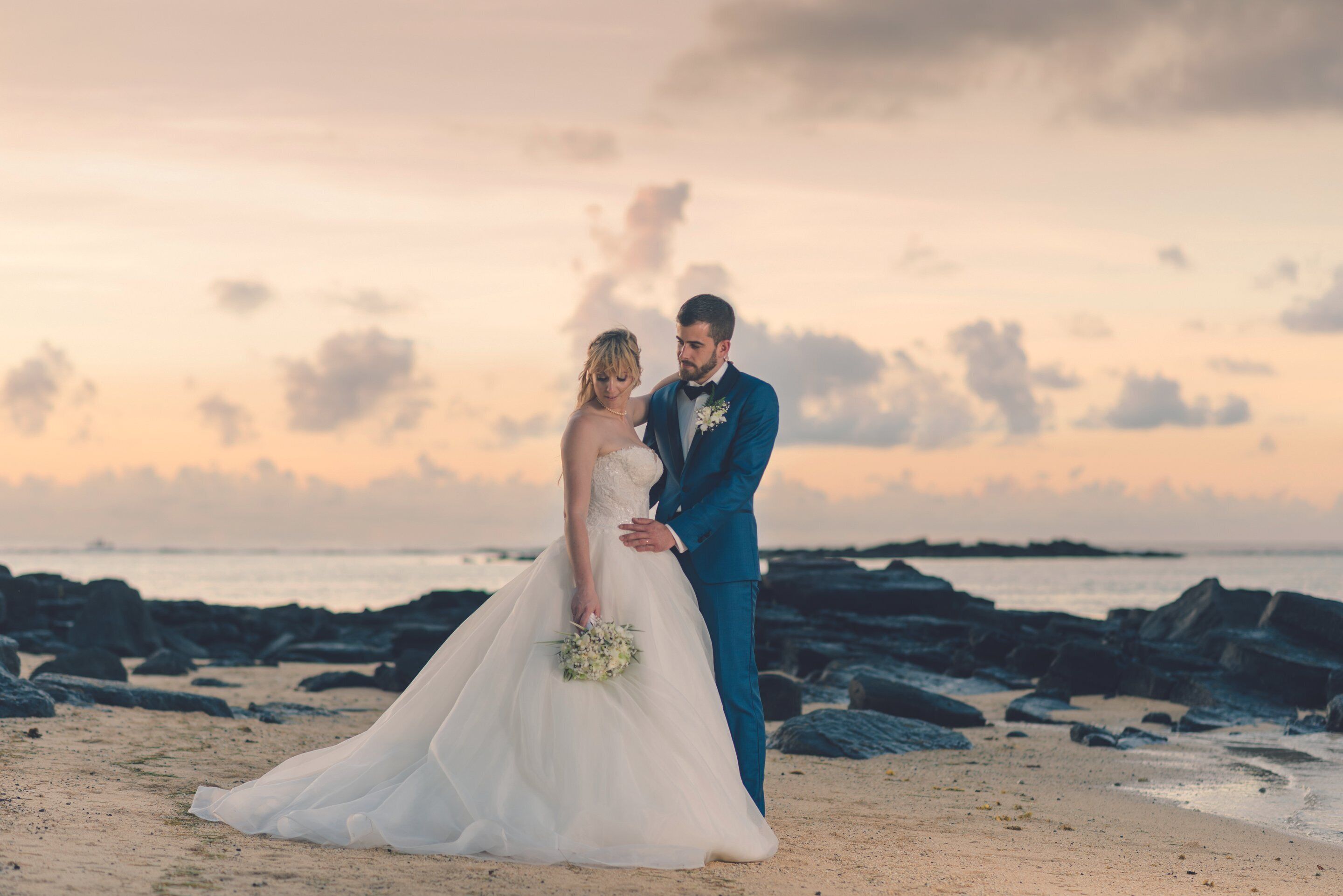 Escena de una boda en la playa, con una novia en un vestido blanco y un novio en traje azul.