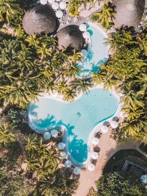 Luftaufnahme eines Resorts mit einem herzförmigen Pool, umgeben von Palmen und Strohdächern.
