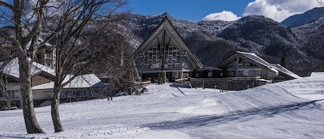 A snow-covered landscape with a lodge featuring a prominent triangular roof and a ski slope in the background.