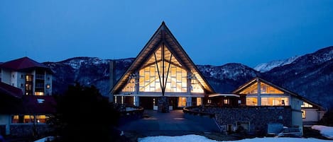 A large, triangular building with a central glass facade, surrounded by snow-covered mountains.