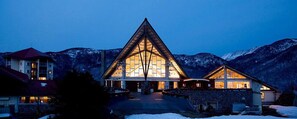 Un grand bâtiment triangulaire doté d’une façade centrale en verre, entouré de montagnes enneigées.