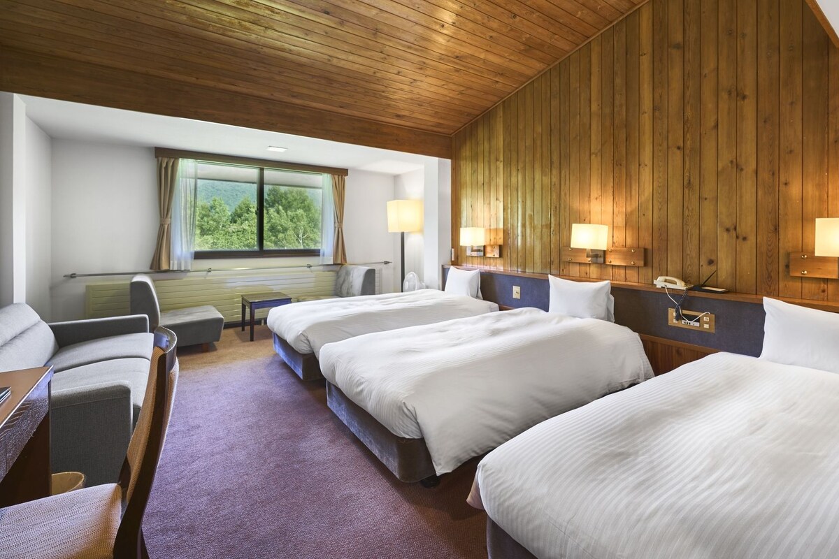 Une chambre d’hôtel avec deux lits, un bureau, une chaise, une fenêtre donnant sur un beau paysage et des murs recouverts de lambris en bois.
