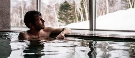 Una persona en un jacuzzi con vistas a árboles cubiertos de nieve.