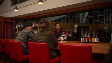A bar area with a wooden counter, red chairs, and bottles of alcohol.