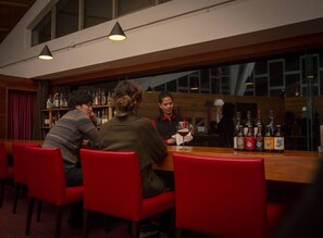 Una zona de bar con mostrador de madera, sillas rojas y botellas de alcohol.