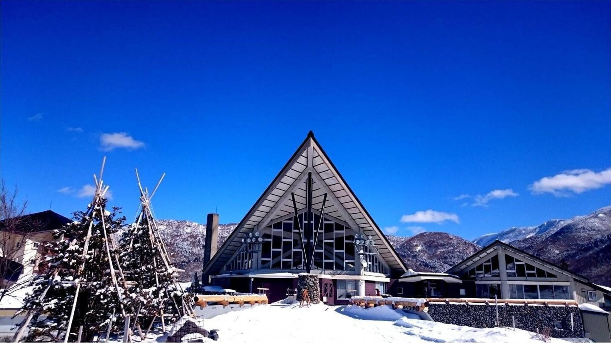 A modern building with a triangular roof and large windows, surrounded by snow-covered mountains.