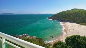 A coastal landscape with a beach, rocky shoreline, and a forested hill. - Apa Pau Brasil (Búzios)