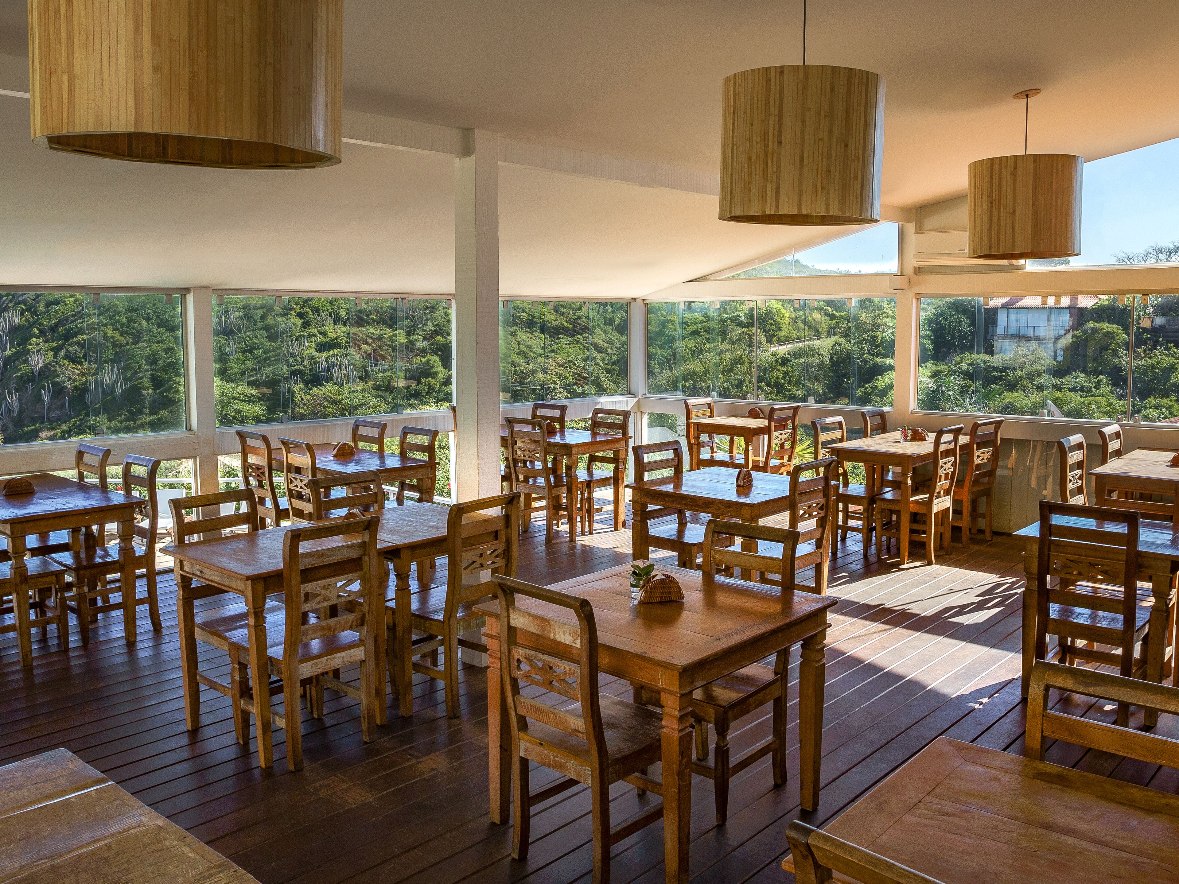 An outdoor dining area with wooden tables and chairs, large windows offering a view of the surrounding greenery.