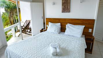 Un dormitorio amplio con una cama grande, cabecera de madera y vistas a un balcón con mobiliario exterior.