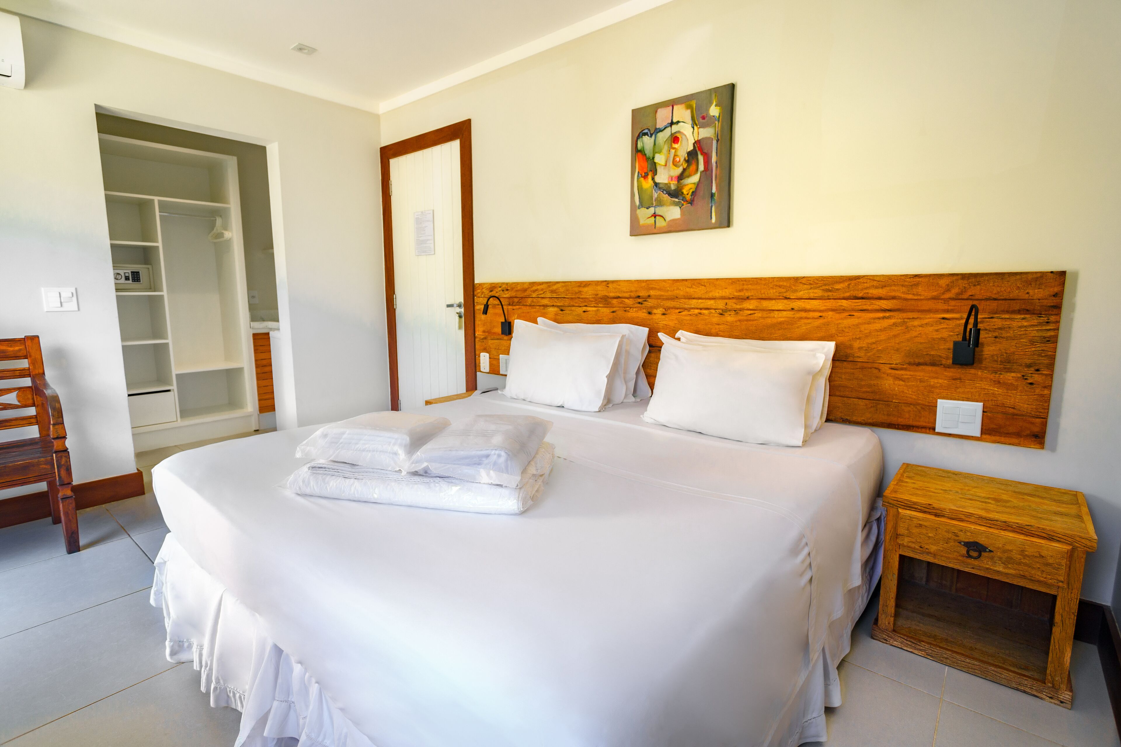 A neatly made bed with white linens and towels, a wooden headboard, a bedside table with a lamp, and a closet with sliding doors.