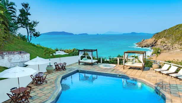 A pool area with lounge chairs, umbrellas, and a view of the ocean. - Apa Pau Brasil (Búzios)