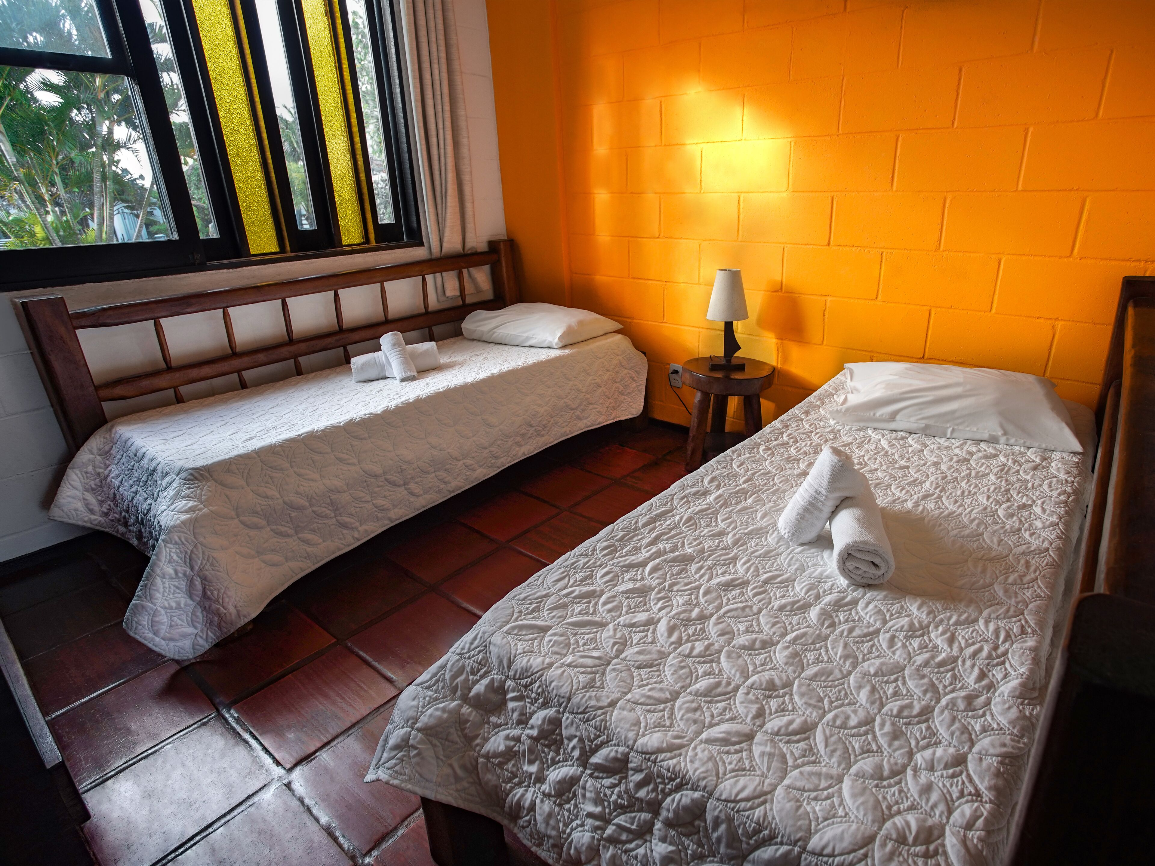 Una habitación de hotel con dos camas, una ventana con cortinas, una lámpara y una pared de ladrillo.