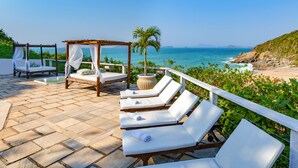 A beachside patio with a wooden canopy bed, lounge chairs, and a view of the ocean. - Apa Pau Brasil (Búzios)