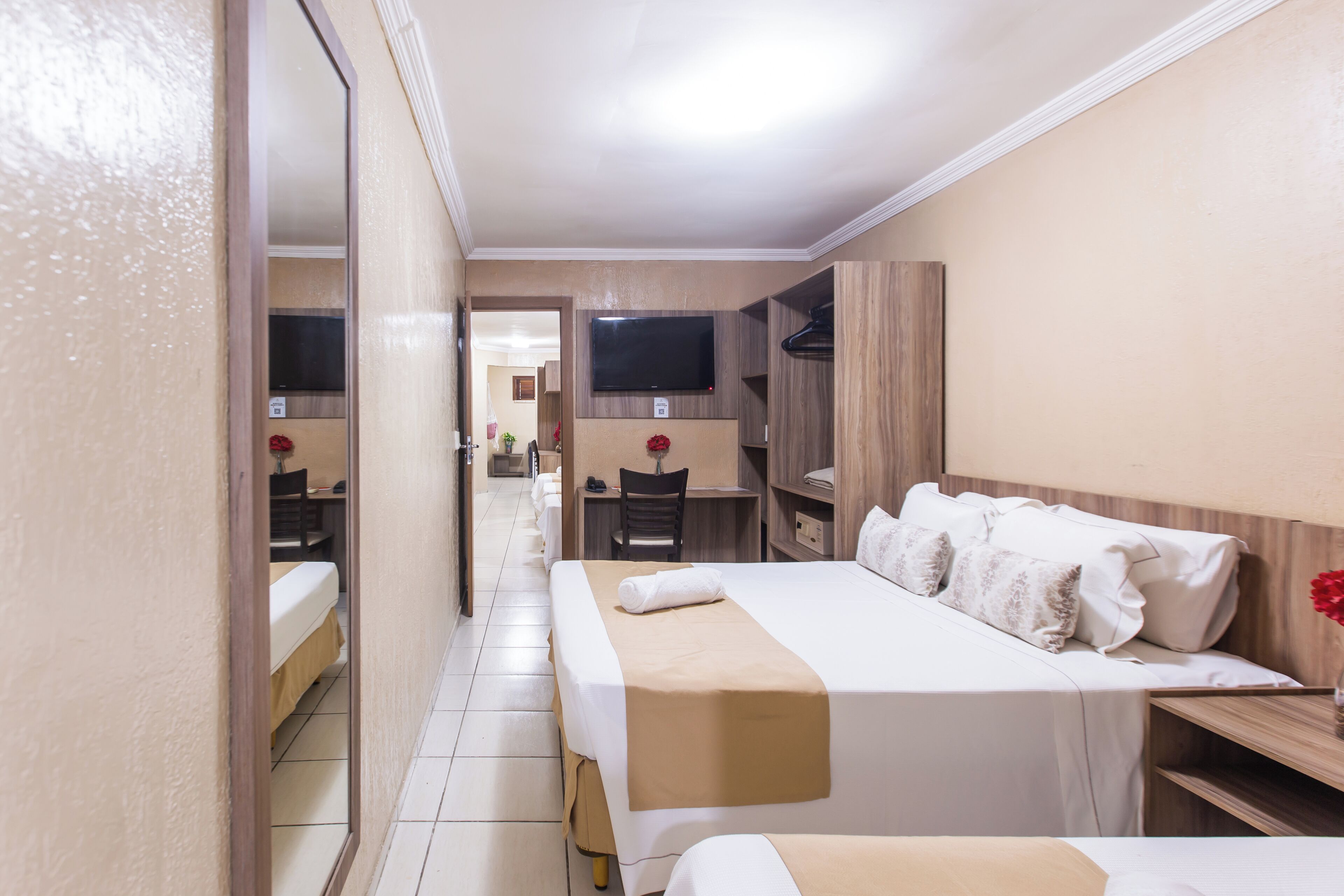 Habitación de hotel con una cama grande, un escritorio, una silla, un televisor montado en la pared y un espejo en la pared izquierda.