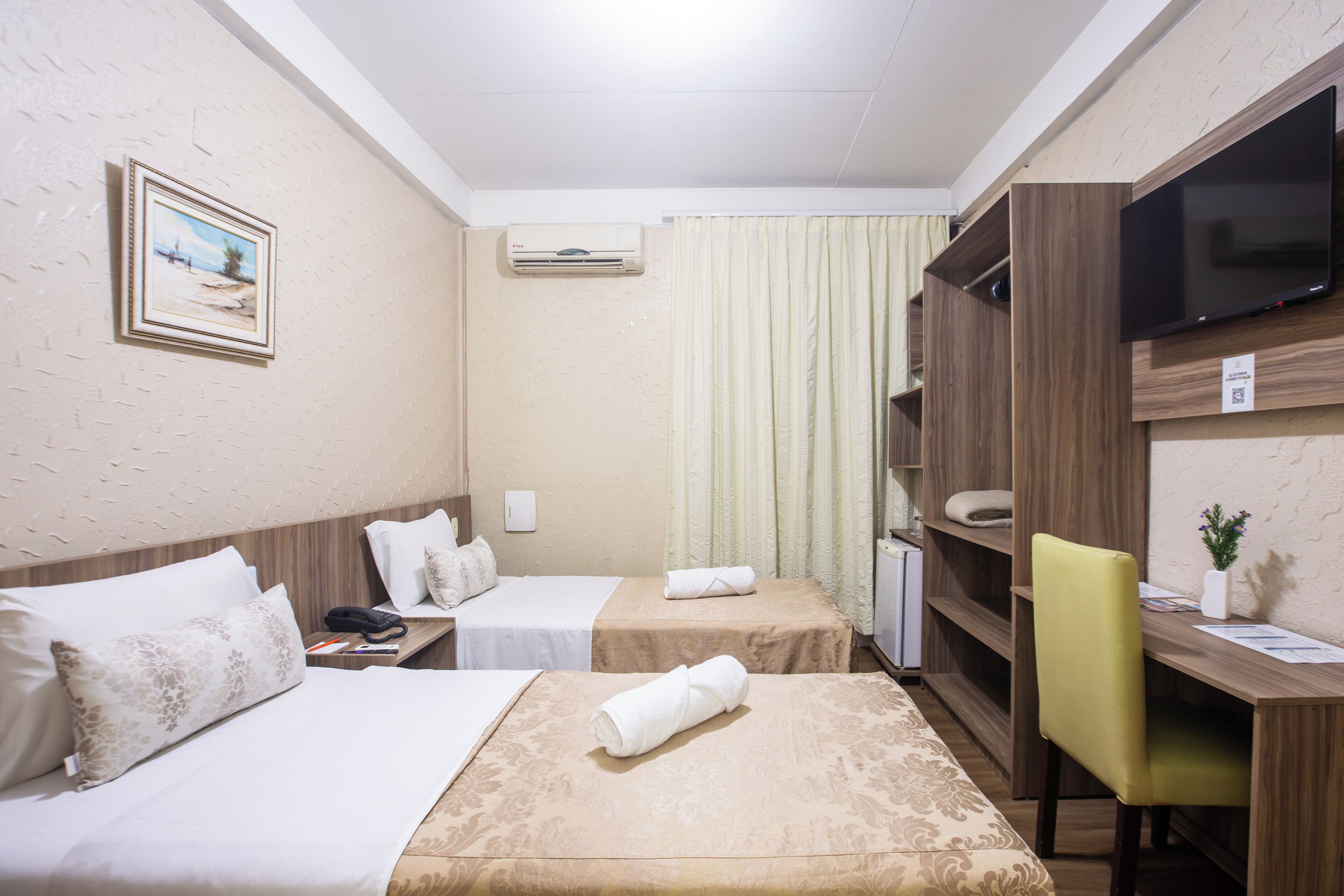 Una habitación de hotel con dos camas, un escritorio, una silla, un televisor y un equipo de aire acondicionado.