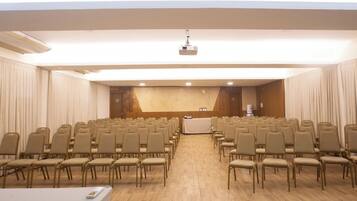 Un salón de conferencias con filas de sillas, un escenario con un atril y un proyector.