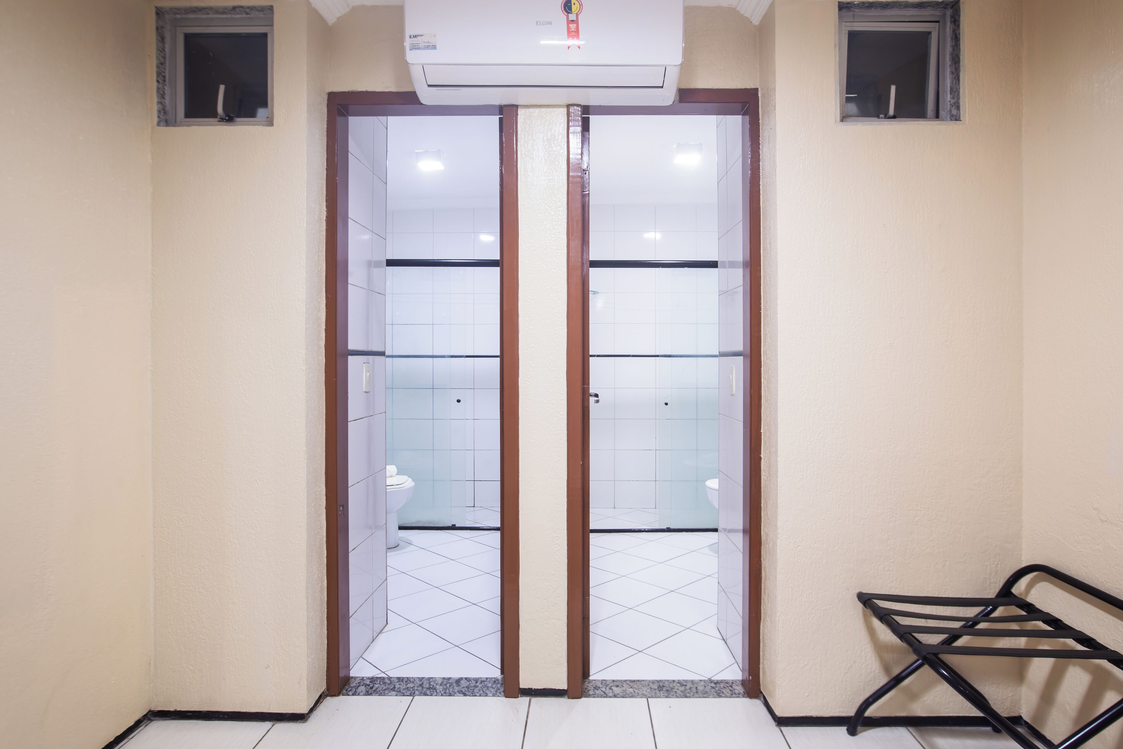 A bathroom with a glass door, white tiled walls, and a ceiling-mounted air conditioner.