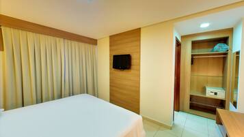 Quarto de hotel com cama, televisão fixada na parede, guarda-roupa e uma pequena mesa.
