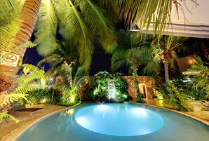 Piscina rodeada de plantas tropicales y una cascada.