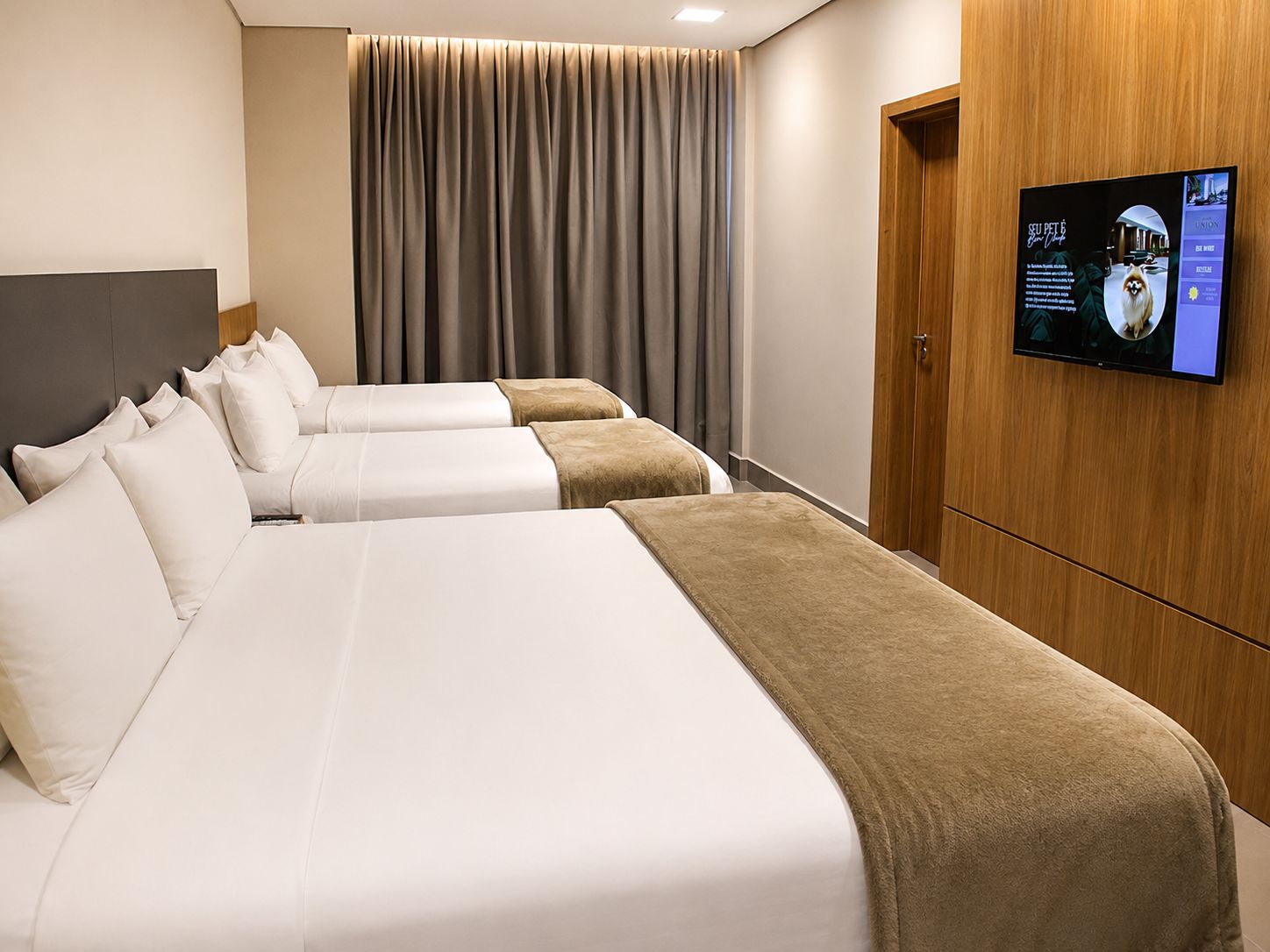 Habitación de hotel con tres camas, televisión y armario de madera.