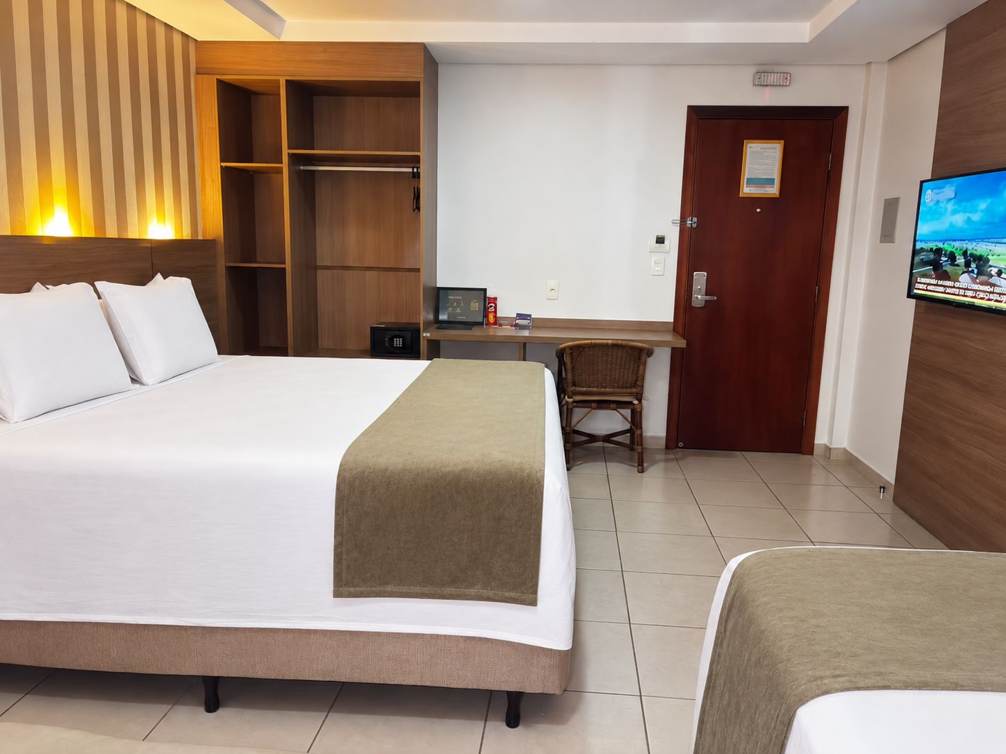 A hotel room with a large bed, a desk with a chair, a television, and a wardrobe.