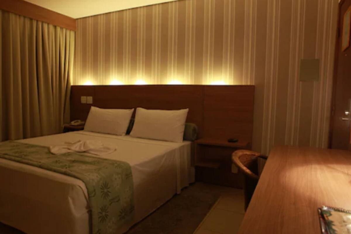 Une chambre d’hôtel avec un lit, une table de chevet, un bureau en bois et une chaise.