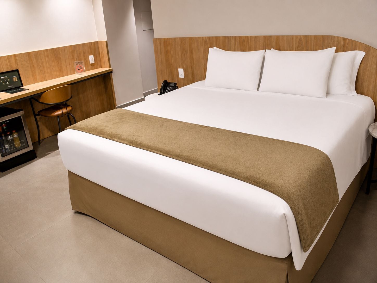 A hotel room with a large bed, a desk with a computer, and a minibar.