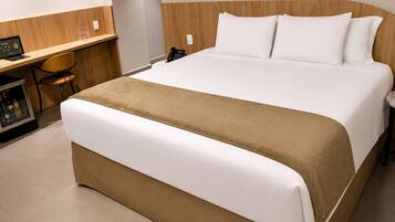 A hotel room with a large bed, a desk with a computer, and a minibar.