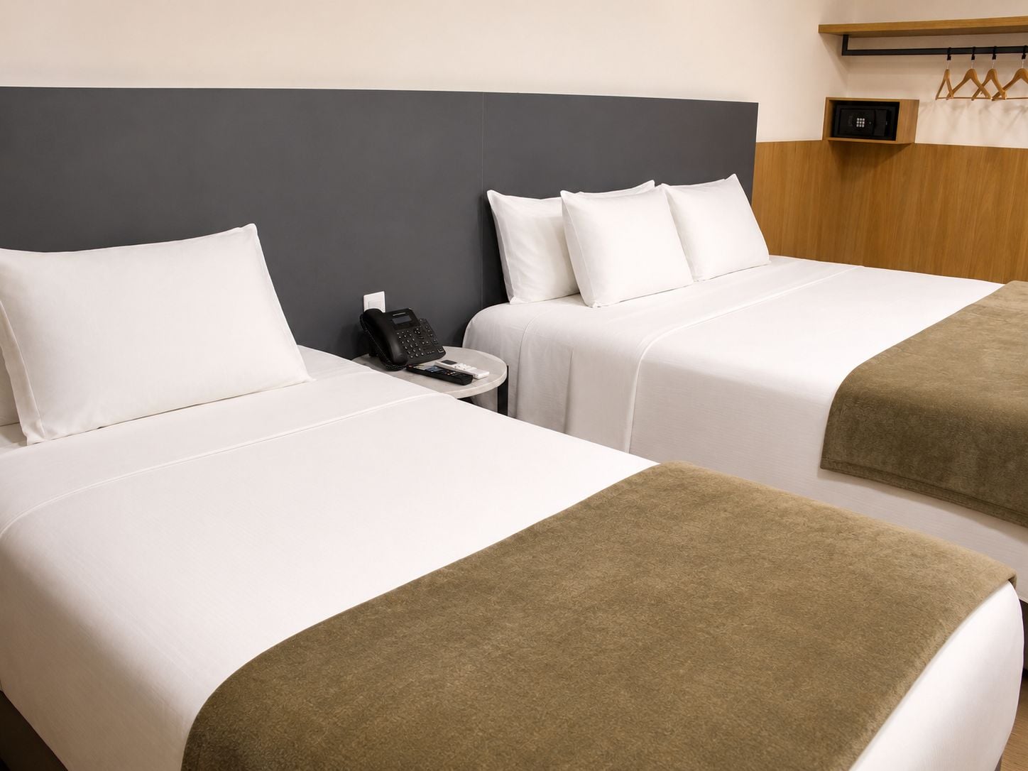 Habitación de hotel con dos camas, una mesita de noche con teléfono y un pequeño estante con caja fuerte.