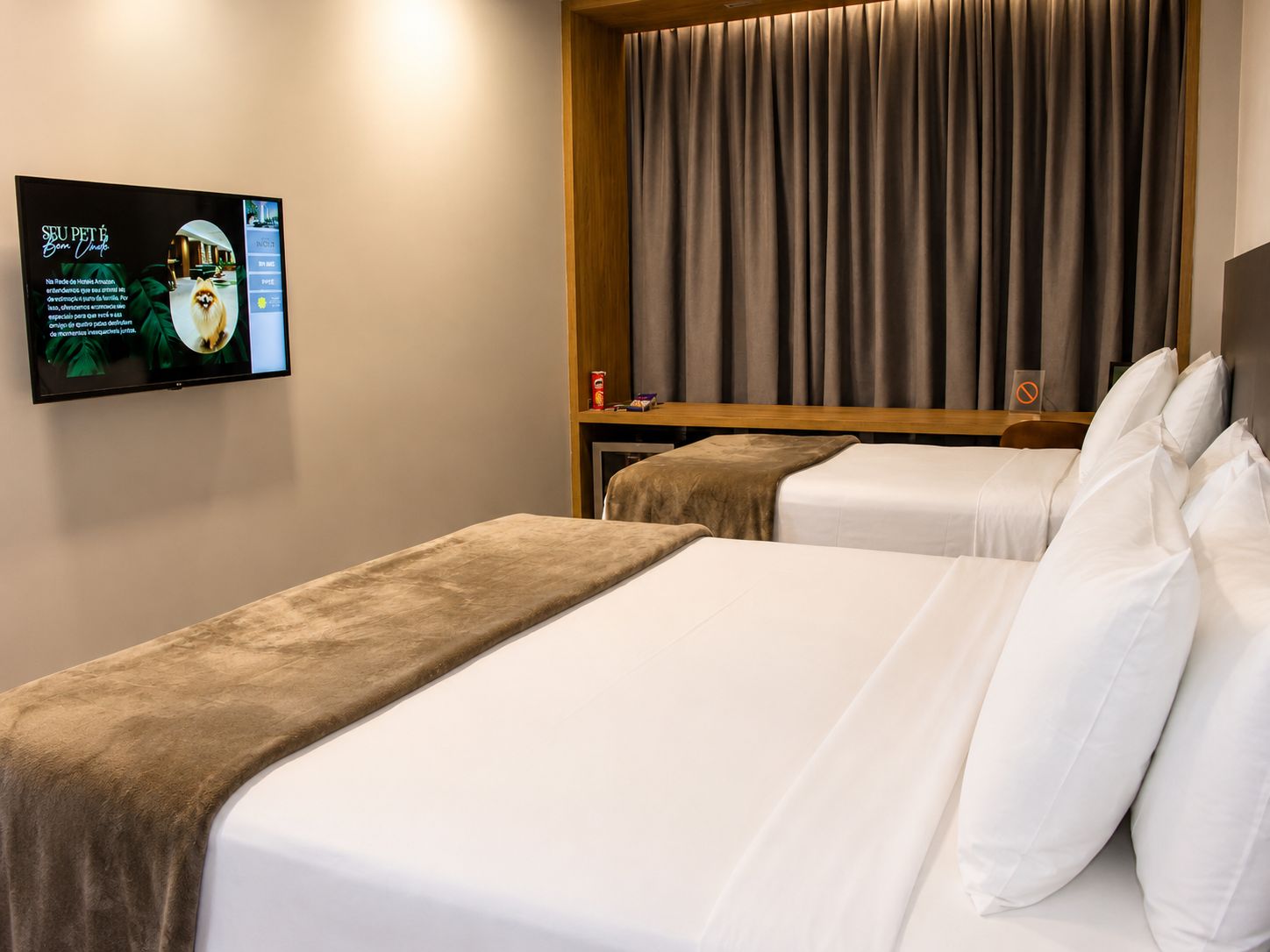 Habitación de hotel con dos camas, un televisor montado en la pared y una cortina cubriendo la ventana.