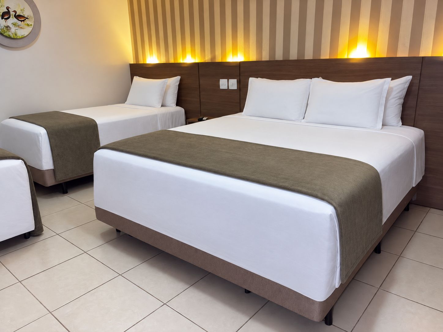 A hotel room with two single beds and one double bed, all with white bedding and brown headboards.