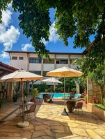 Zona junto a la piscina con mobiliario exterior y sombrillas, piscina y un edificio con techo de tejas.